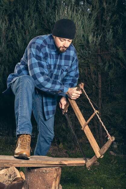 Photo full length of lumberjack cutting plank from saw against trees at forest