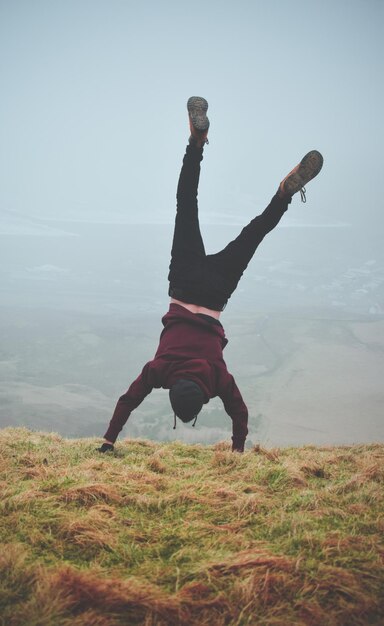 Foto lunghezza intera di un uomo che fa handstand sull'erba contro il cielo