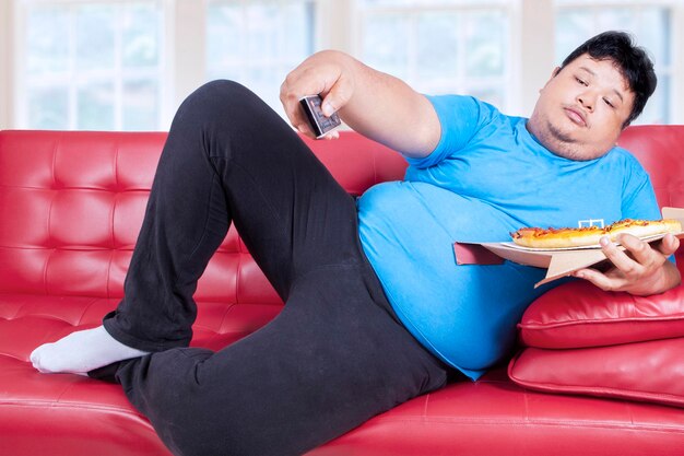 Photo full length of man eating pizza while relaxing on sofa at home