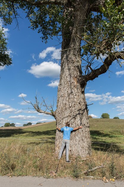 Foto lunghezza intera di un uomo che abbraccia il tronco di un albero contro il cielo