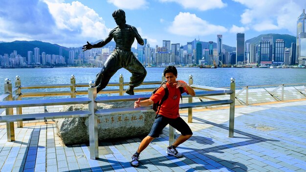 Foto lunghezza intera di un uomo che fa un gesto contro una statua in città durante una giornata di sole