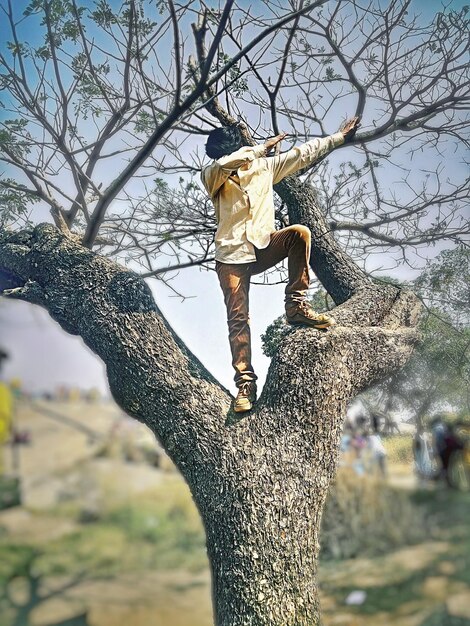 Foto lunghezza intera di un uomo che fa un gesto mentre è in piedi su un albero nudo