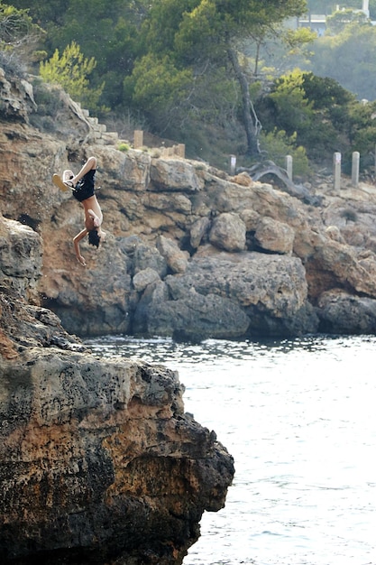 Foto lunghezza completa di un uomo che salta in mare da una roccia