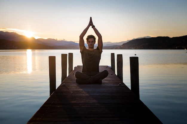 Photo full length of man mediating on pier against sky during sunset