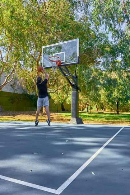 Foto lunghezza intera di un uomo che gioca a basket contro gli alberi