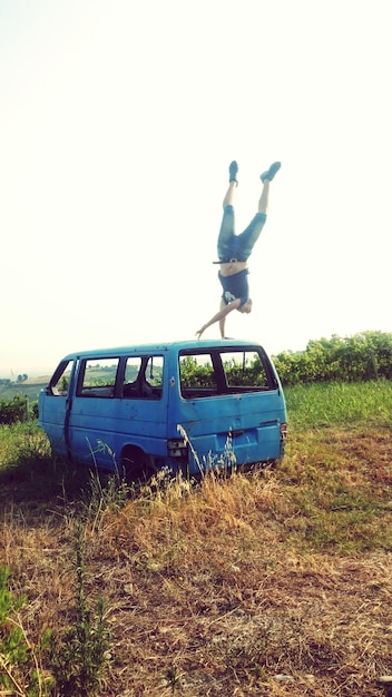 Foto lunghezza completa di un uomo che pratica il handstand su un furgone abbandonato contro un cielo limpido