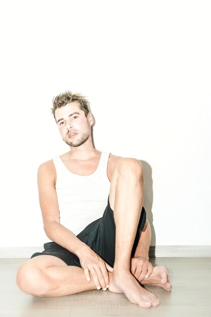 Photo full length of man sitting against white wall at home