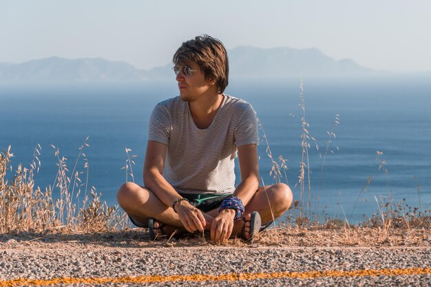 Photo full length of man sitting on land against sea and sky