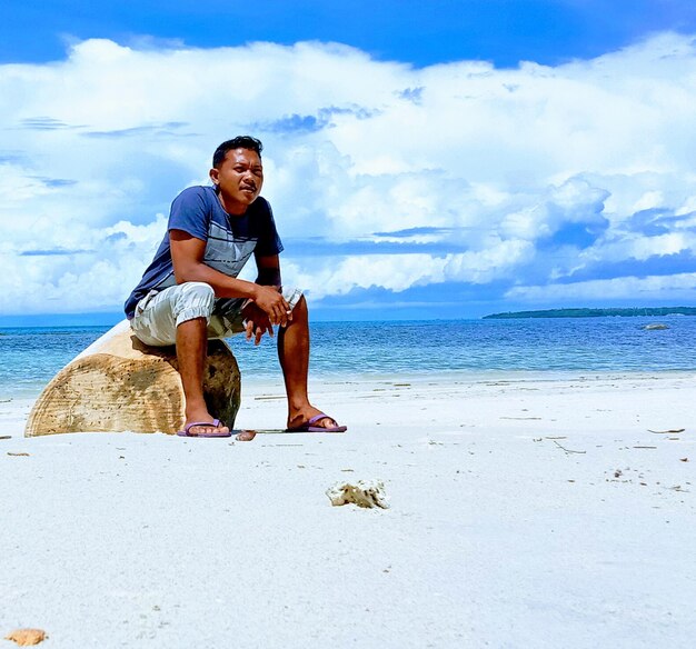 Full length of man sitting on shore at beach against sky