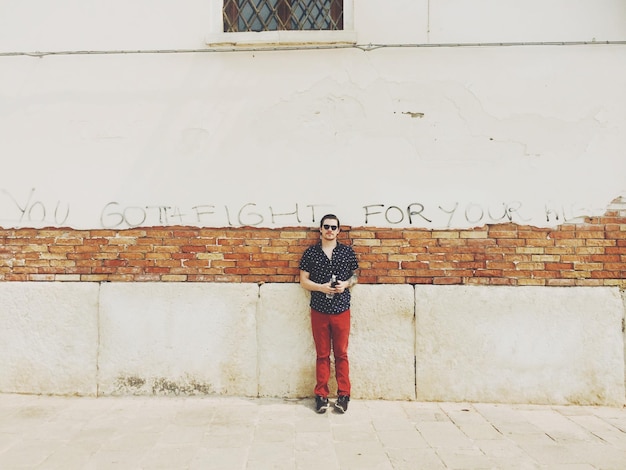 Photo full length of man standing by damaged wall with message