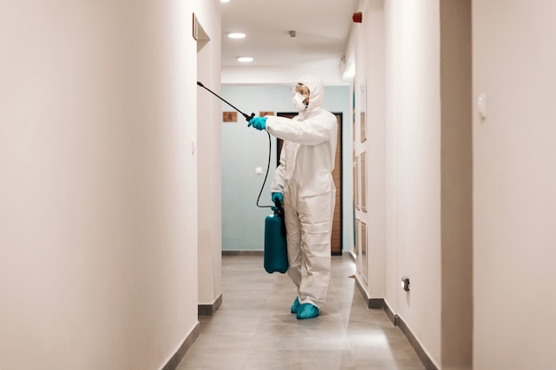 Full length of man in sterile suit disinfecting hall of the building. Protection from corona concept.