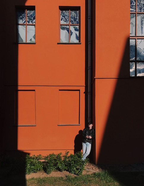 Full length of man using mobile phone while standing against building