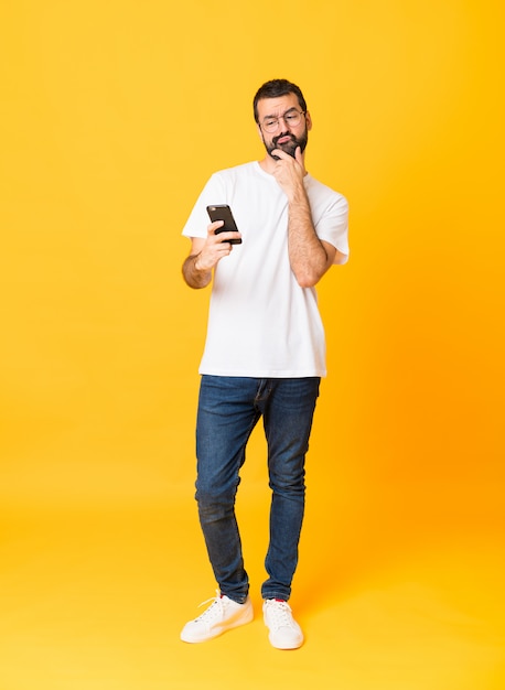 Полная длина человек с бородой над изолированной желтой стеной мышления и отправки сообщения