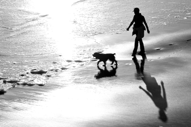 Foto lunghezza completa di un uomo con un cane che cammina sulla spiaggia