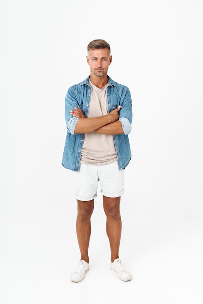 Full length of masculine guy in denim shirt keeping arms crossed and looking at you isolated on white