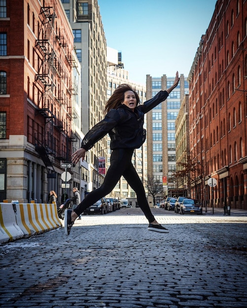 Полная длина зрелой женщины с вытянутыми руками прыгает на улице против зданий в городе