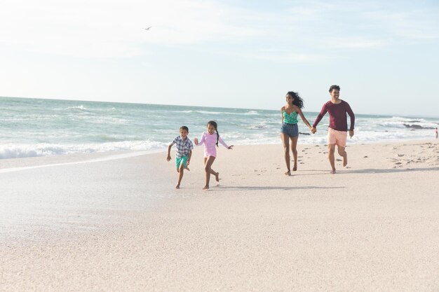 Photo full length of multiracial parents following behind children running on shore at beach against sky