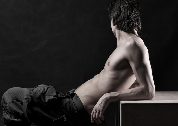 Full length of a naked young man posing against black background