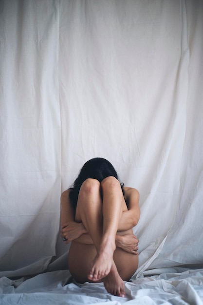 裸の若い女性がベッドに座って織物を背負っている全長