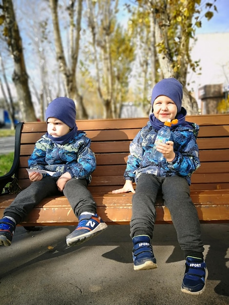 Фото Полная длина мальчика в теплой одежде, сидящего на скамейке в парке