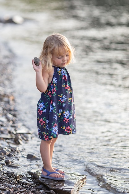 사진 강변에서 돌을 들고 있는 귀여운 소녀의 전체 길이