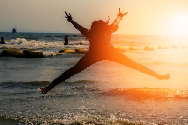Фото Полная длина возбужденной девушки, прыгающей на пляже во время захода солнца.