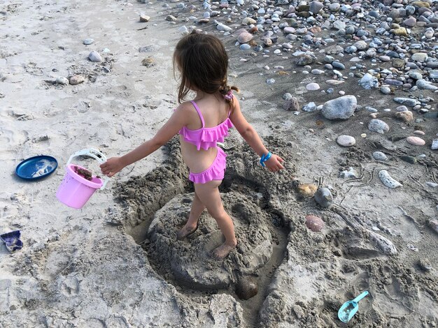 写真 ビーチで砂の刻をしている女の子の全長
