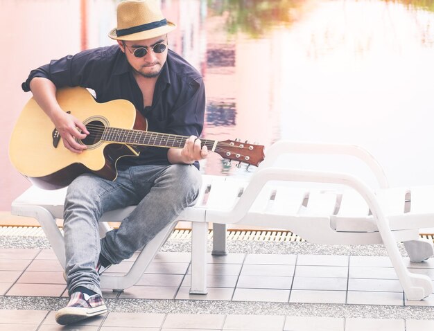 写真 外で座ってギターを弾いている男の全長