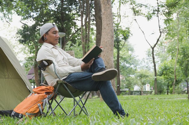 写真 テントの草の上に椅子に座って本を読んでいる男の全長