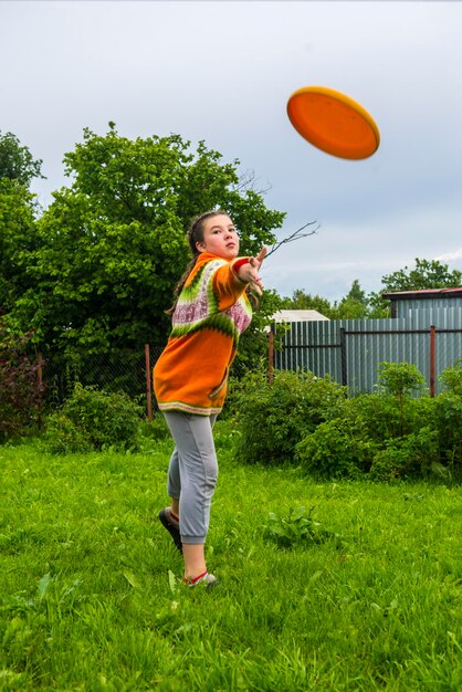 写真 庭に立ってプラスチックのディスクを投げる遊び心のある女の子の全長