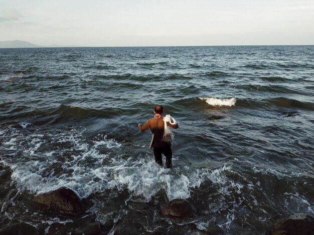 Фото Человек без рубашки, стоящий в море напротив неба.