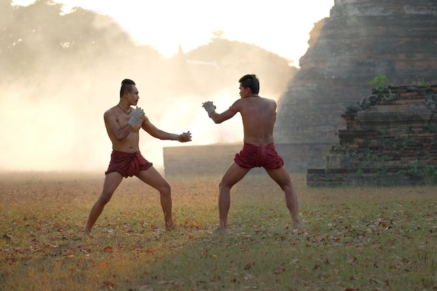 写真 シャツのない男が空に逆らって地面でボクシングしている