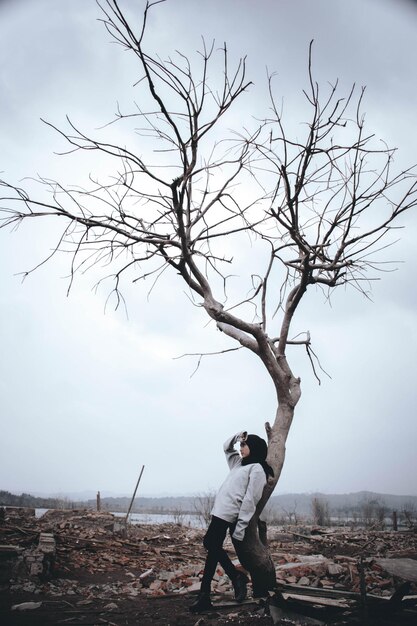 写真 空に向かって裸の木に寄りかかっている女性の全長