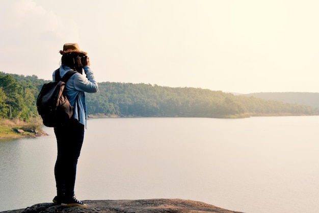 写真 明るい空に照らされた森林の近くの湖を写真に撮る女性の長さ