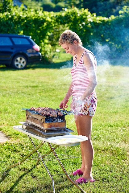 写真 庭のバーベキューグリルで肉を調理している女性の全長