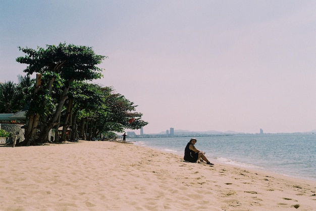 Фото Полная длина женщины, сидящей на пляже против неба