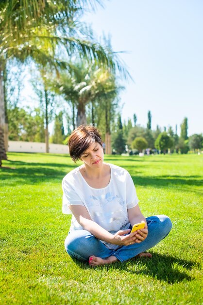 写真 公園に座っている間スマートフォンを使用している女性の全長