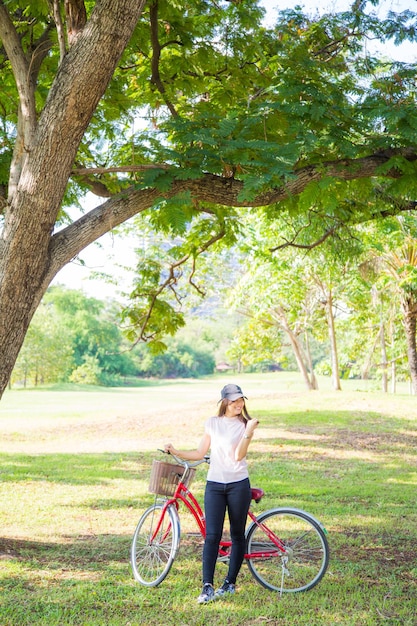 写真 樹木の近くの畑に立っている自転車の女性の全長