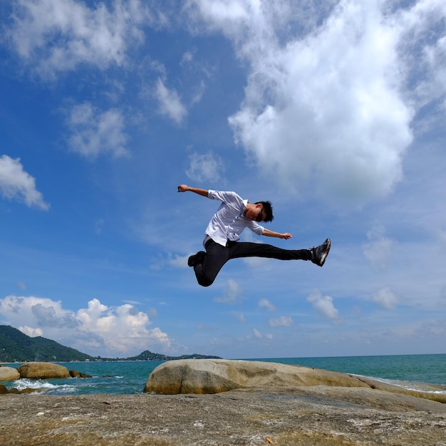 写真 海と空に向かってジャンプする若者の全長