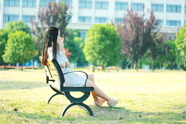 写真 公園のベンチに座っている若い女性の全長