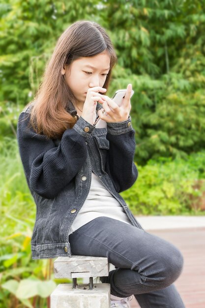 사진 밖에서 앉아있는 동안 전화를 사용하는 젊은 여성의 전체 길이