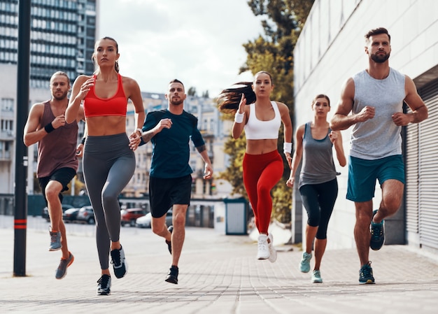 Foto per tutta la lunghezza delle persone in abbigliamento sportivo che fanno jogging mentre si allenano sul marciapiede all'aperto