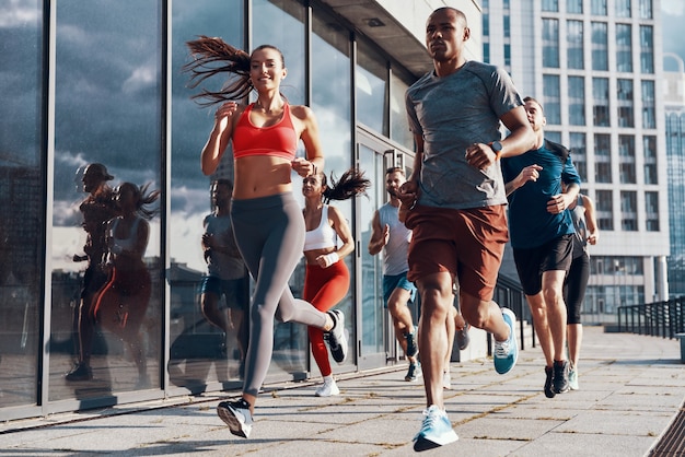 full length of people in sports clothing jogging while exercising on the sidewalk outdoors