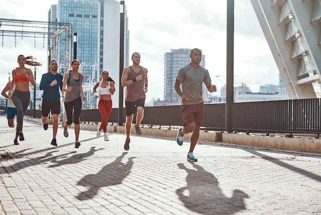 full length of people in sports clothing jogging while exercising on the sidewalk outdoors