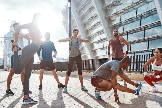 Per tutta la lunghezza delle persone in abbigliamento sportivo che si scaldano e si allungano mentre si esercitano sul marciapiede all'aperto