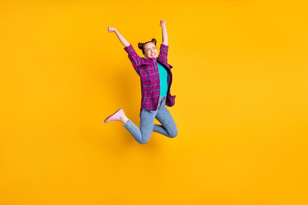 魅力的な狂気の十代の女性の完全な長さの写真は、空中飛行恍惚としたチャンピオンマラソンスポーツ競技会を高くジャンプしますカジュアルな格子縞のシャツの靴ジーンズ分離された黄色の背景
