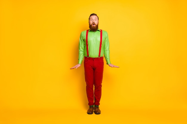 Full length photo of attractive funky guy standing impressed good mood rejoicing wear green shirt red suspenders pants socks footwear isolated bright color