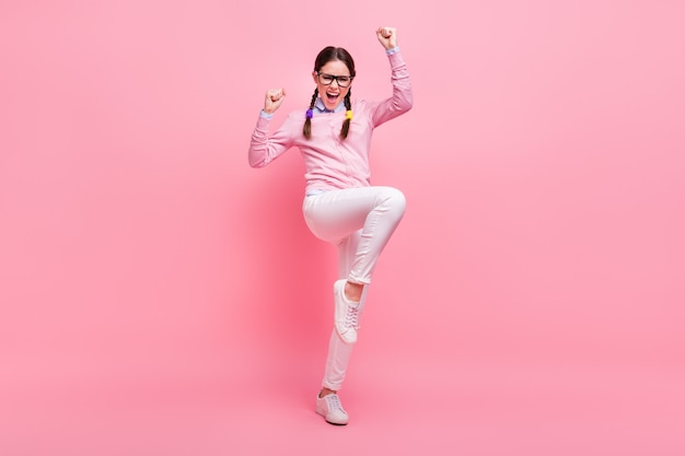 Full length photo of attractive student lady good mood raise fists celebrate excellent grade test exam wear shirt pullover specs trousers footwear isolated pastel pink color background