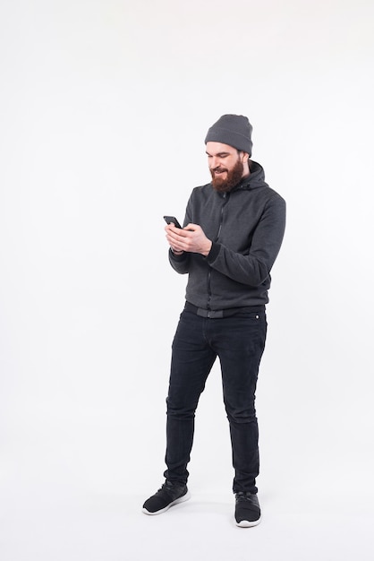 Full length photo of bearded man using smartphone over white