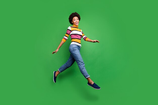 Full length photo of charming funky afro american girl jump go walk on fall weekend holidays wear denim jeans 